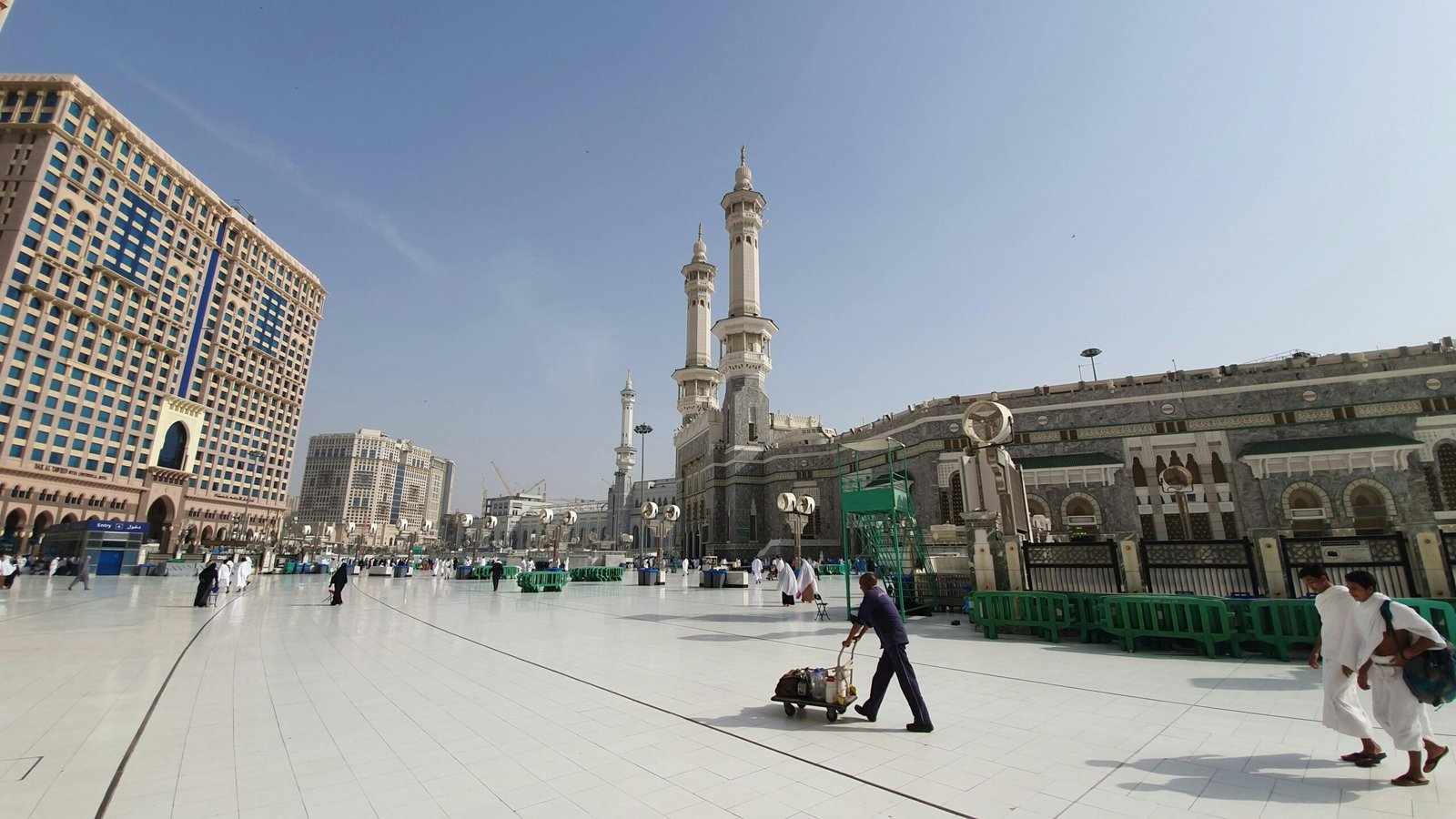 A view of the iconic Masjid Al-Haram in Mecca with pilgrims and nearby buildings.