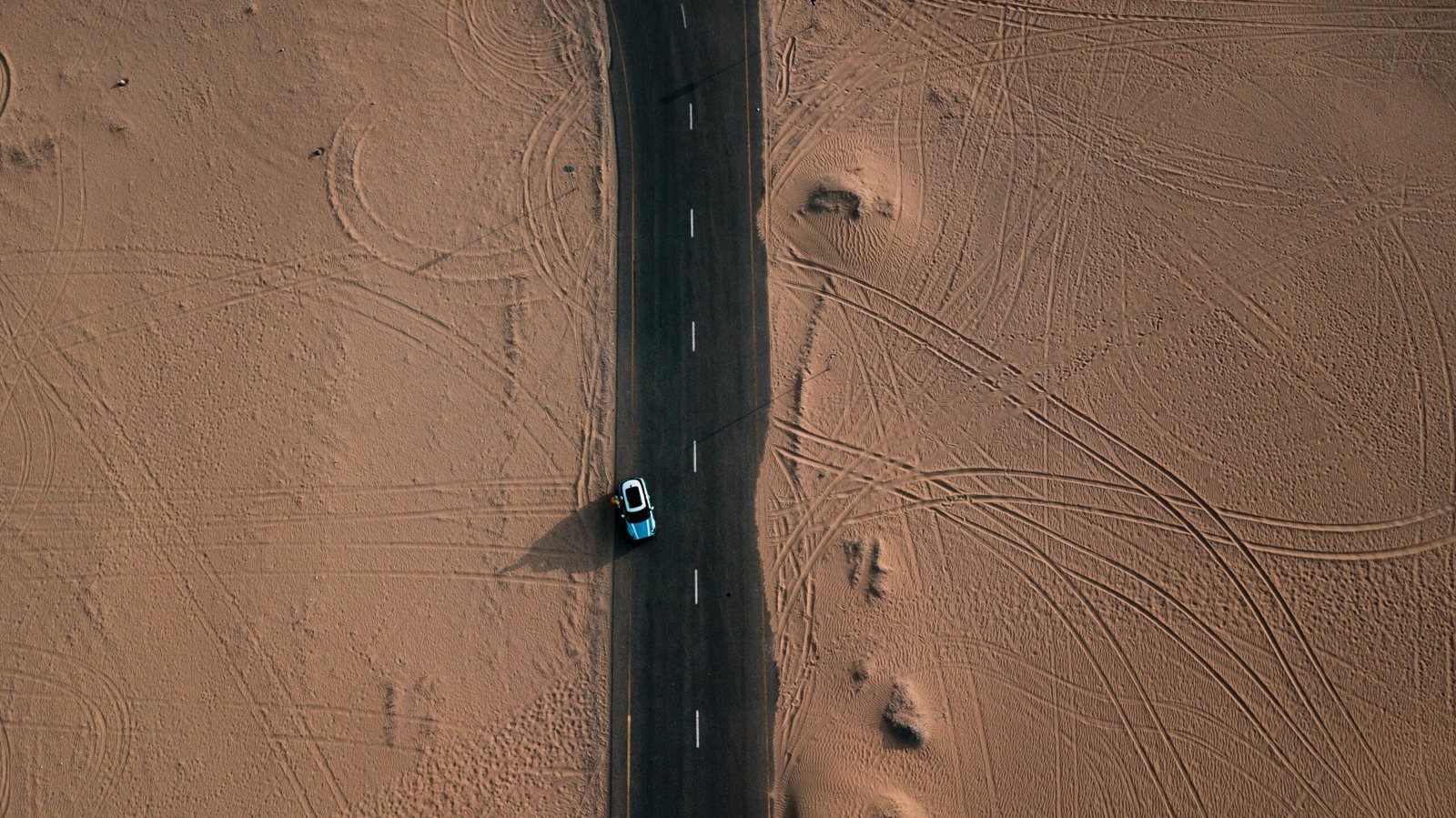 Drone view of a car driving through a desert road in Dubai, UAE.mashaer fleet